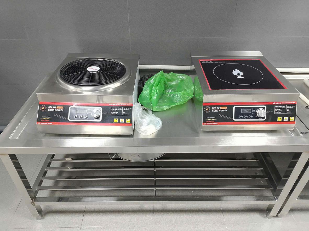 Nhân viên bếp đang dùng khăn và dung dịch chuyên dụng để lau chùi mặt bàn inox sáng bóng.